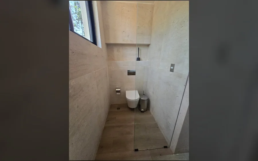 Medio bano con revestimiento claro y puerta de cristal